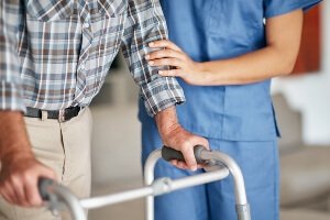 image of a nurse aide helping an elderly man with a walker